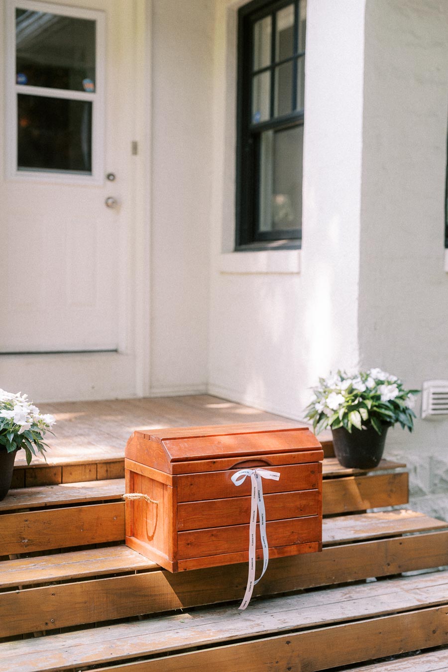 Wooden card box with ribbon on porch steps beside potted flowers.