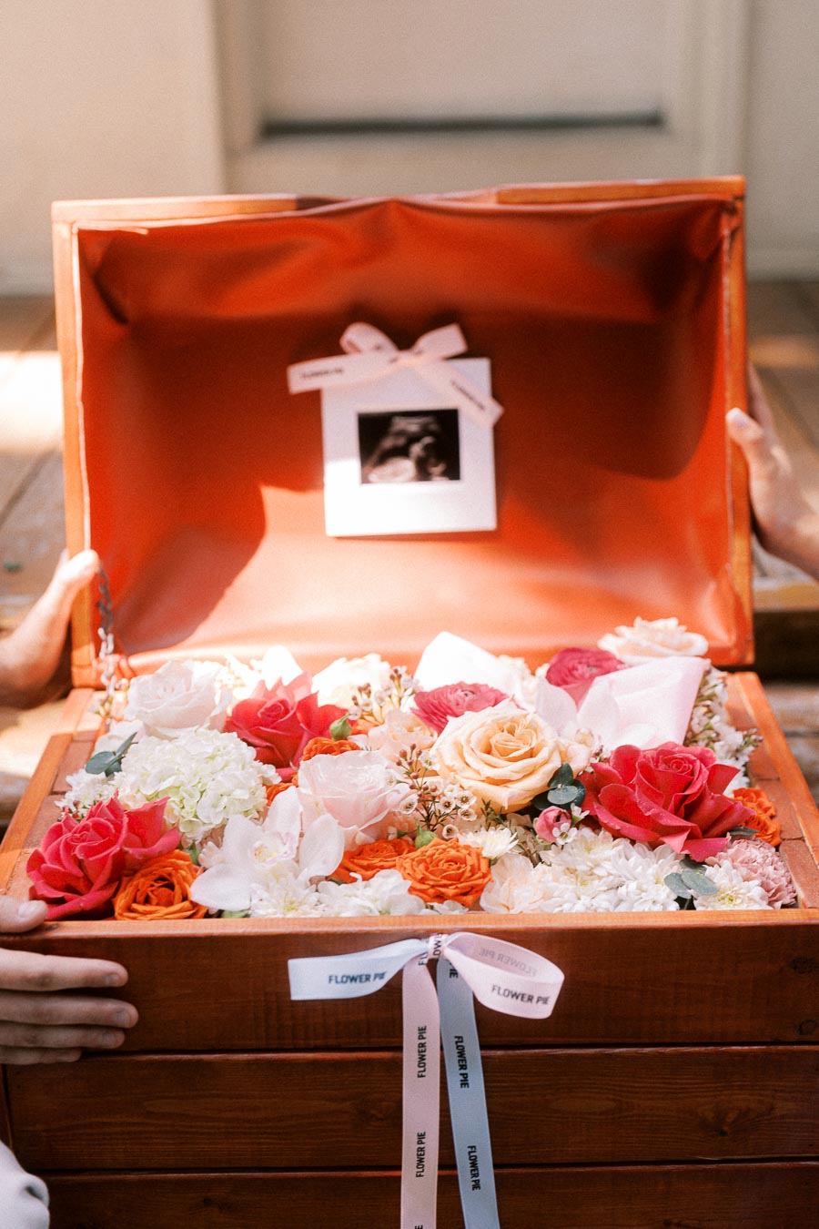 Open wooden flower box filled with roses and a small instant photo inside.