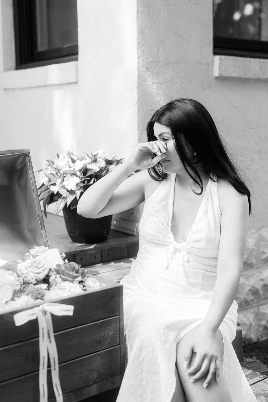 Woman in a white dress wiping tears beside flowers during an engagement session.