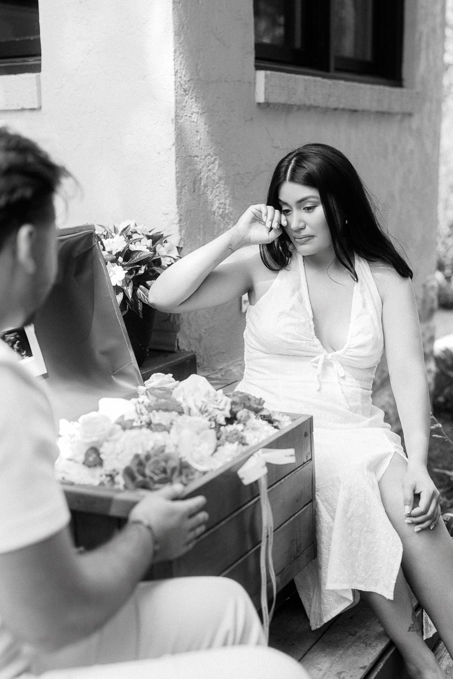 Black and white engagement photo of a woman wiping tears beside flowers.