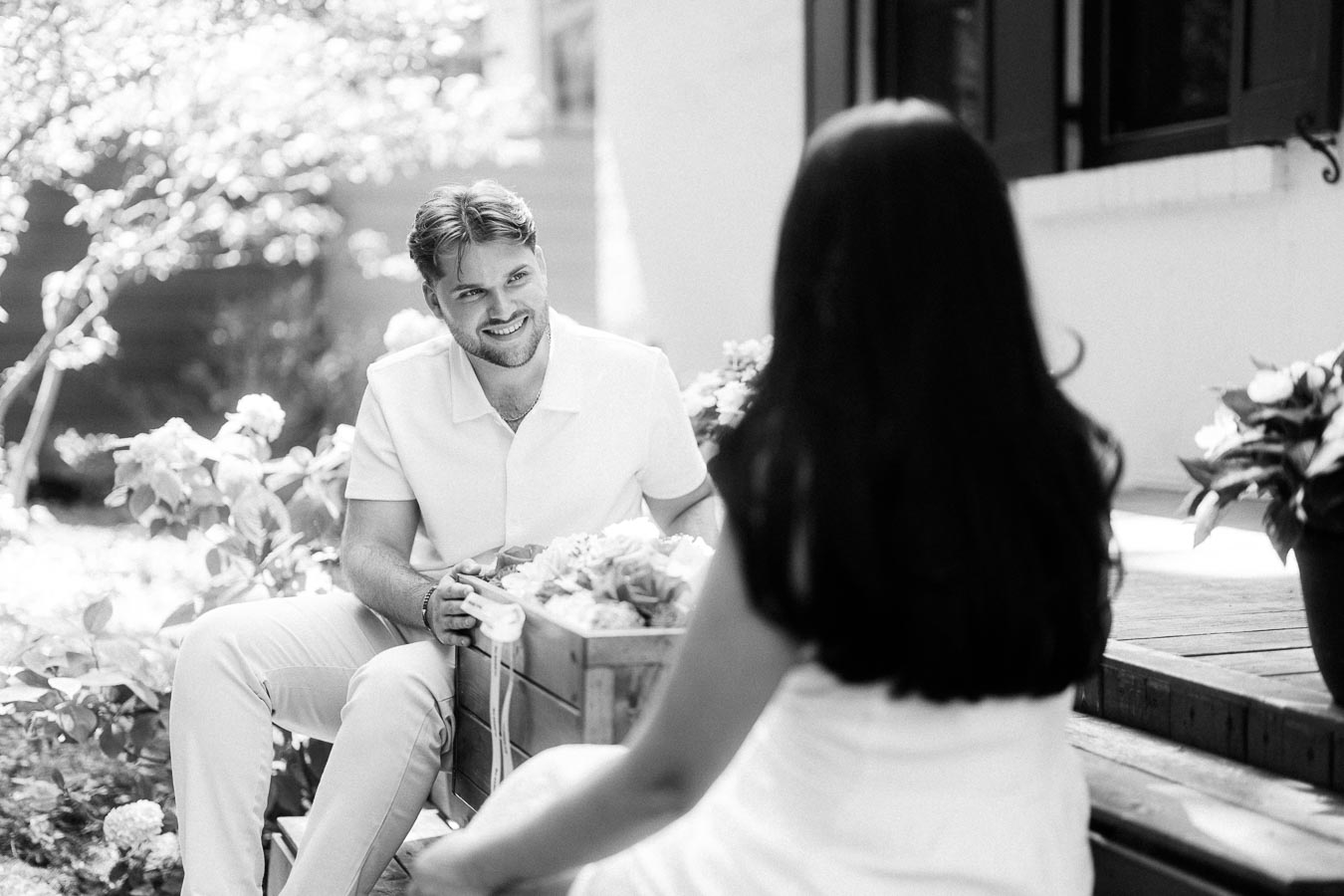 Man smiling at his partner during a black and white garden engagement photo.
