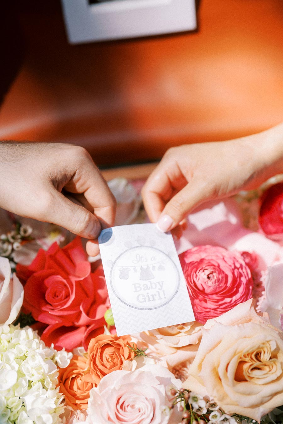 Hands holding a baby girl announcement card above colourful flowers.