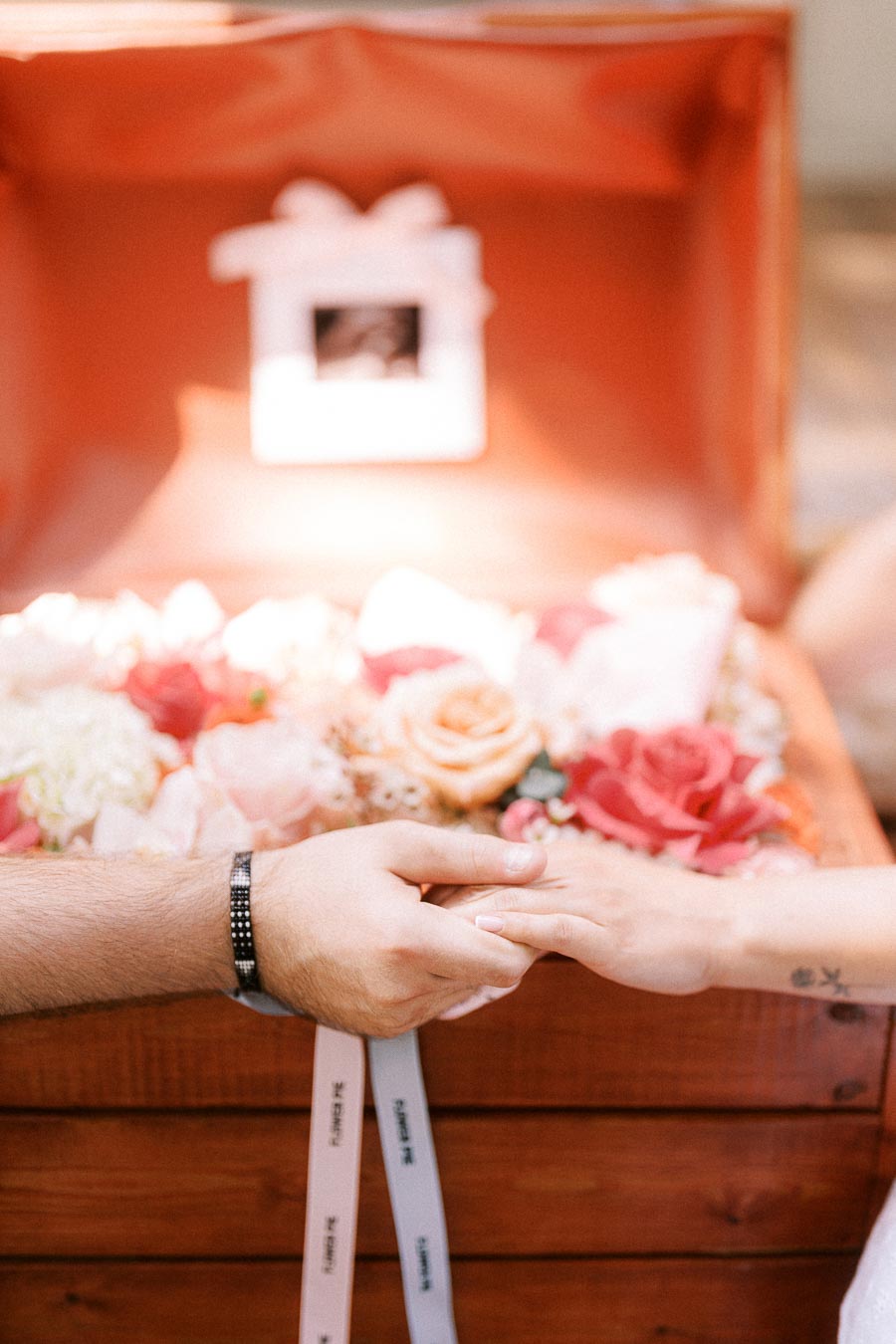 Couple holding hands in front of flowers inside a wooden box.