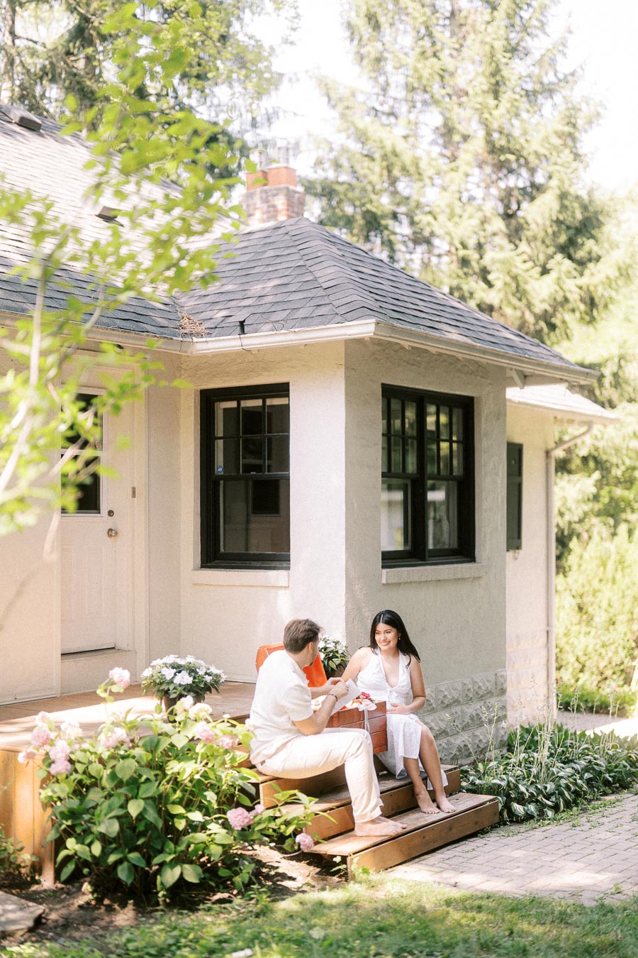 Couple sitting on cottage steps surrounded by garden greenery and flowers.