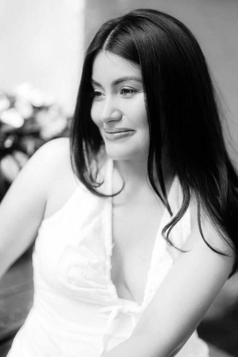 Black and white engagement portrait of a woman in a white dress smiling softly.