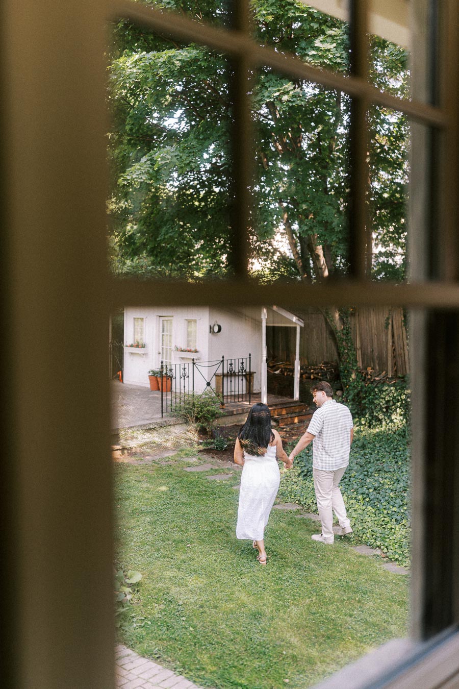 Engaged couple holding hands while walking through a green backyard garden.
