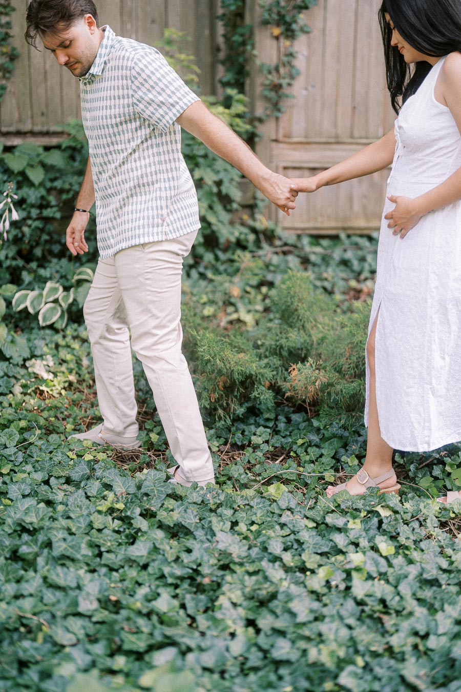 Couple holding hands while walking through a leafy garden during an engagement photo.