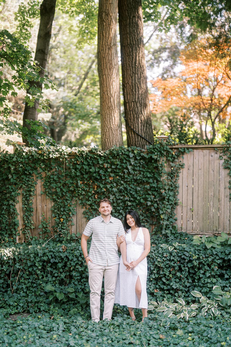 Couple standing together in a leafy garden with ivy and tall trees.