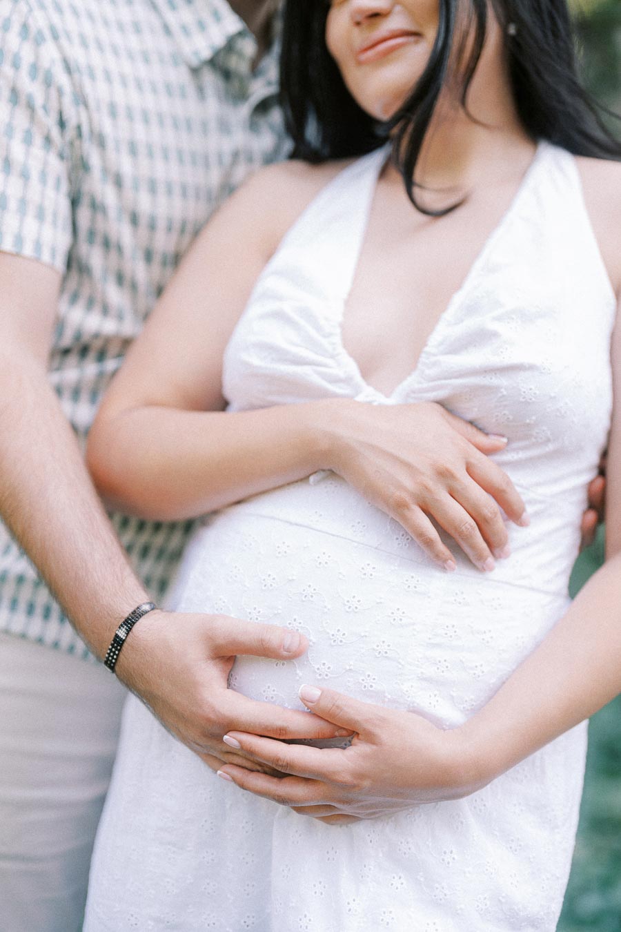 Expectant couple gently holding a baby bump during an engagement photo.