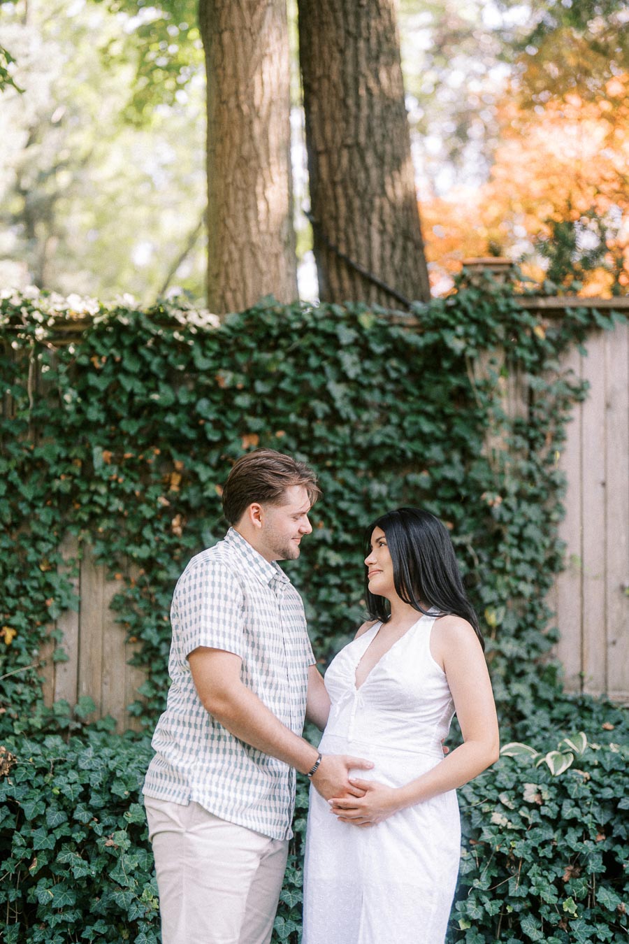 Expectant couple standing together by an ivy-covered fence during an engagement photo.