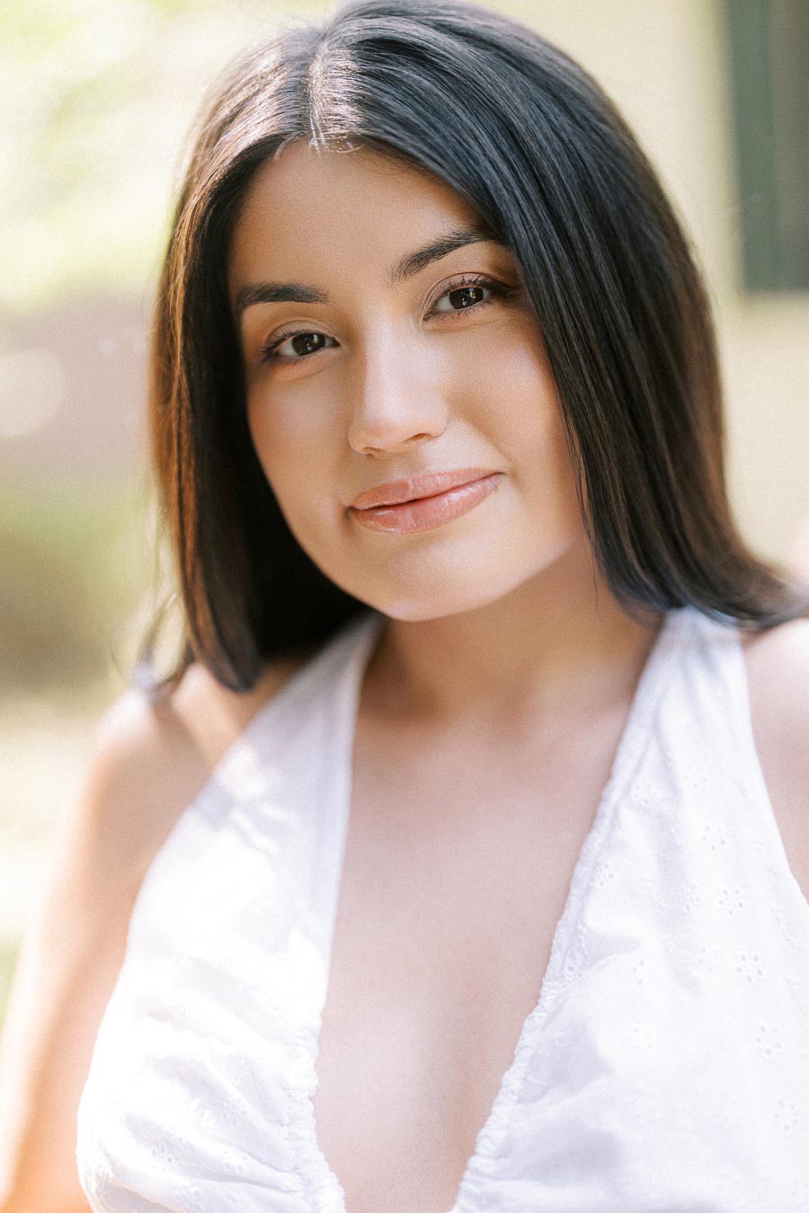 Close-up engagement portrait of a woman in a white sleeveless top outdoors.