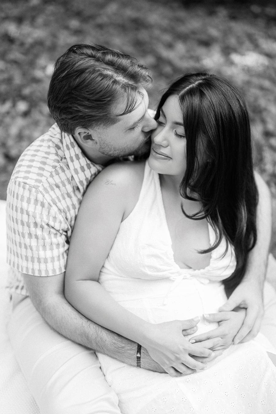 Black and white engagement portrait of a couple embracing as he kisses her cheek.