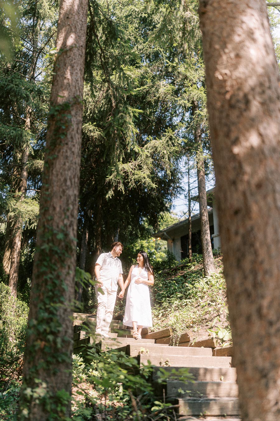 Engaged couple holding hands on wooden steps among tall trees.