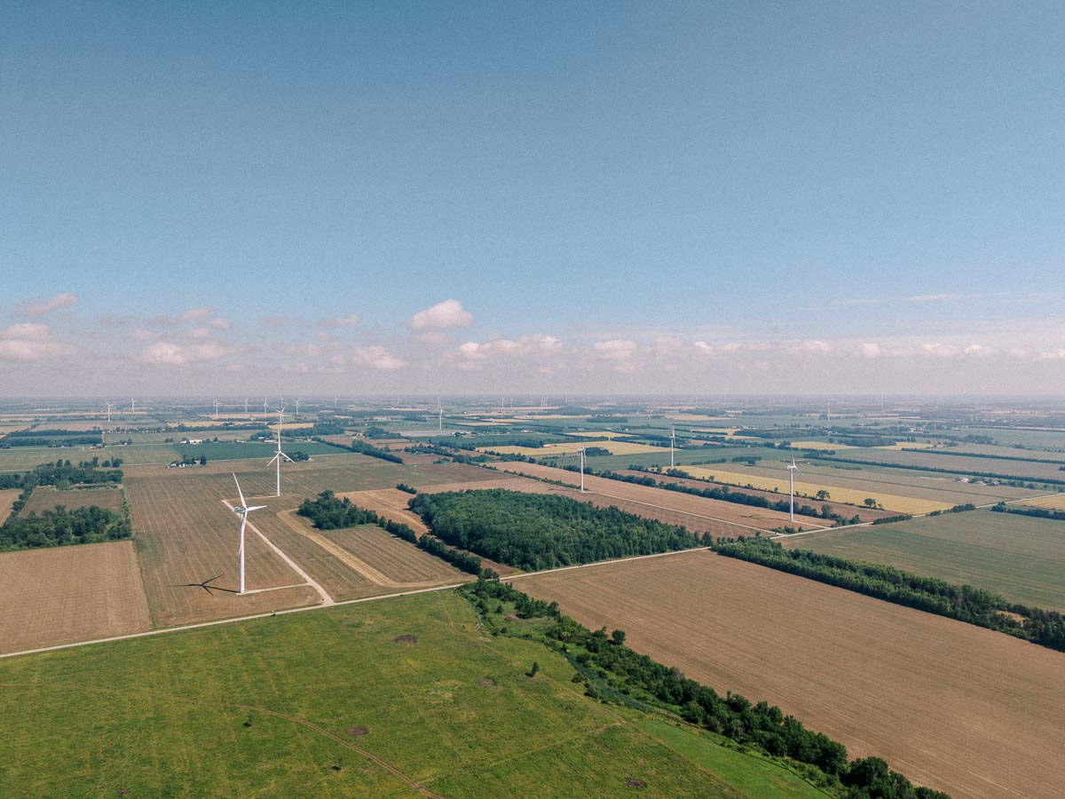 Aerial view of farmland with wind turbines under a blue, lightly clouded sky
