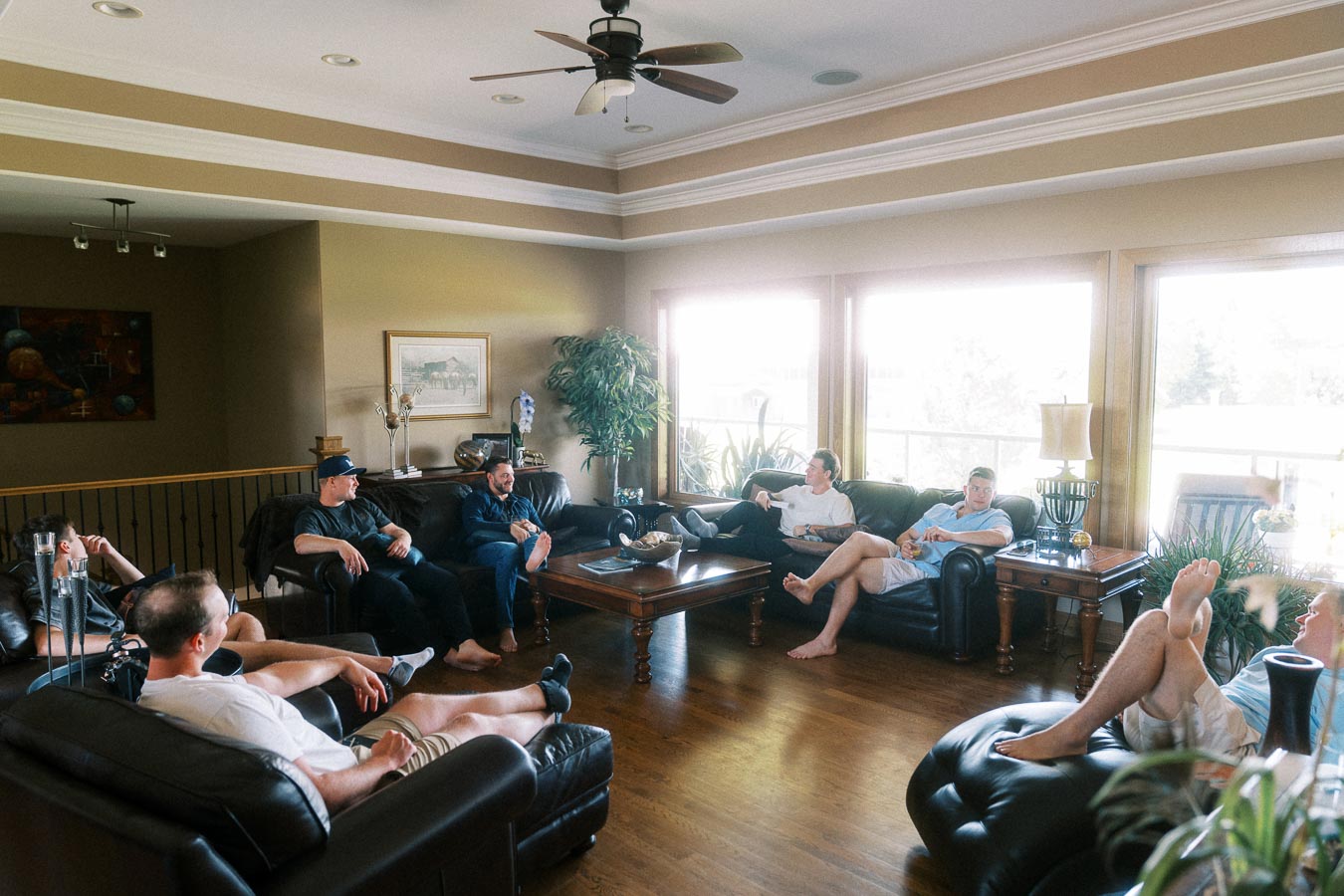 Men relaxing on black leather sofas in a bright living room before a wedding