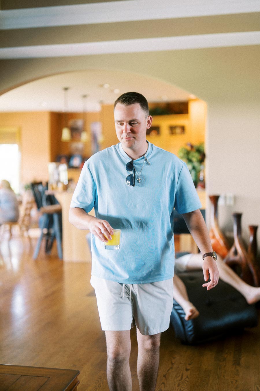 Man in a blue shirt walks through a home holding a drink.