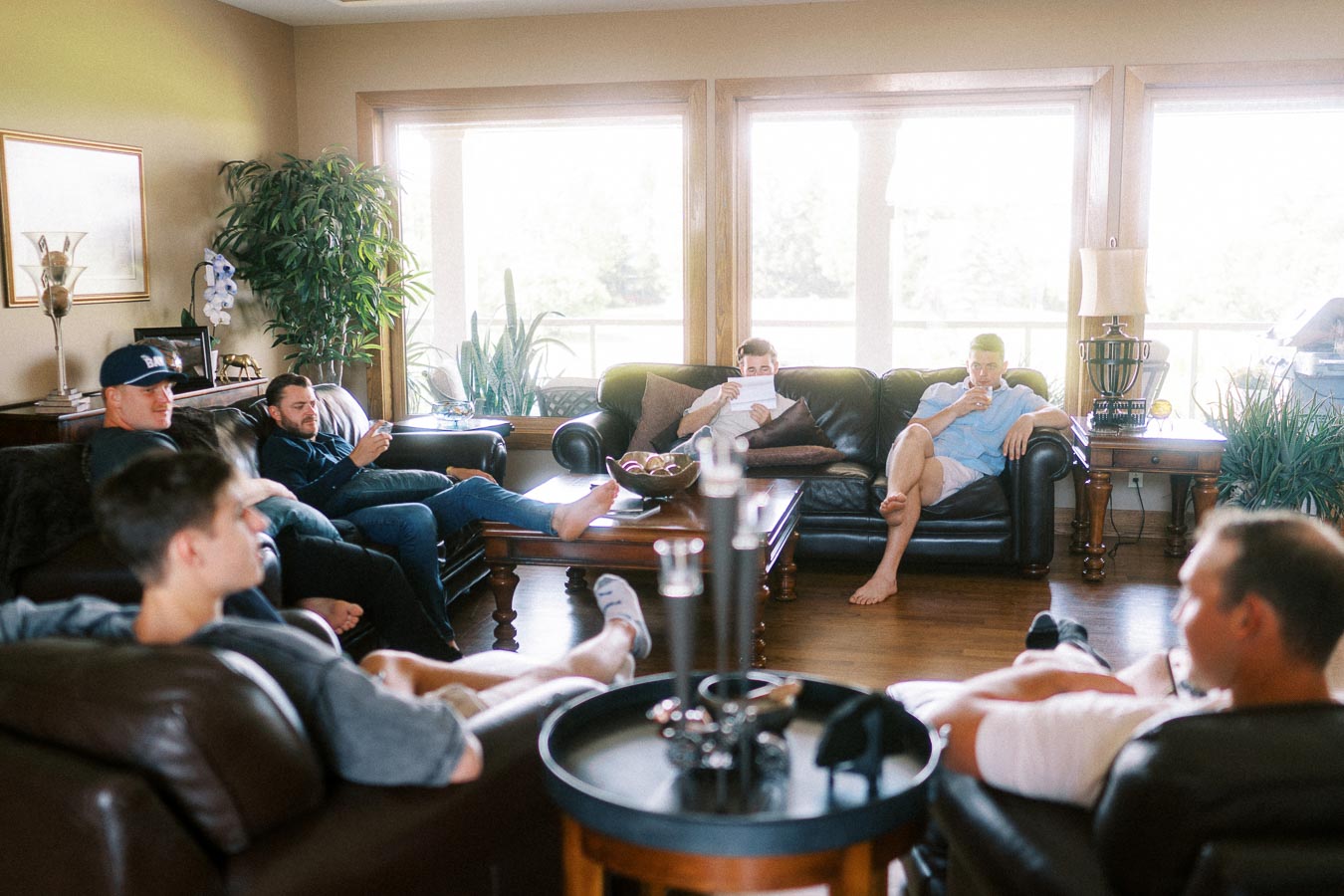 Men relaxing on leather sofas in a bright living room before getting ready.
