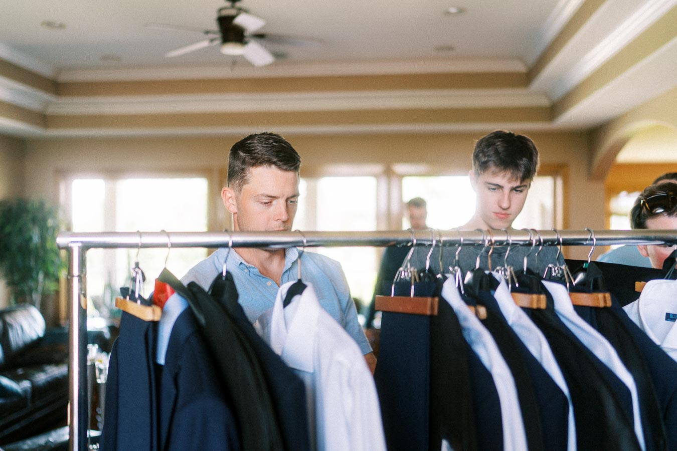 Men browse suits on a clothing rack during groom preparations at home.