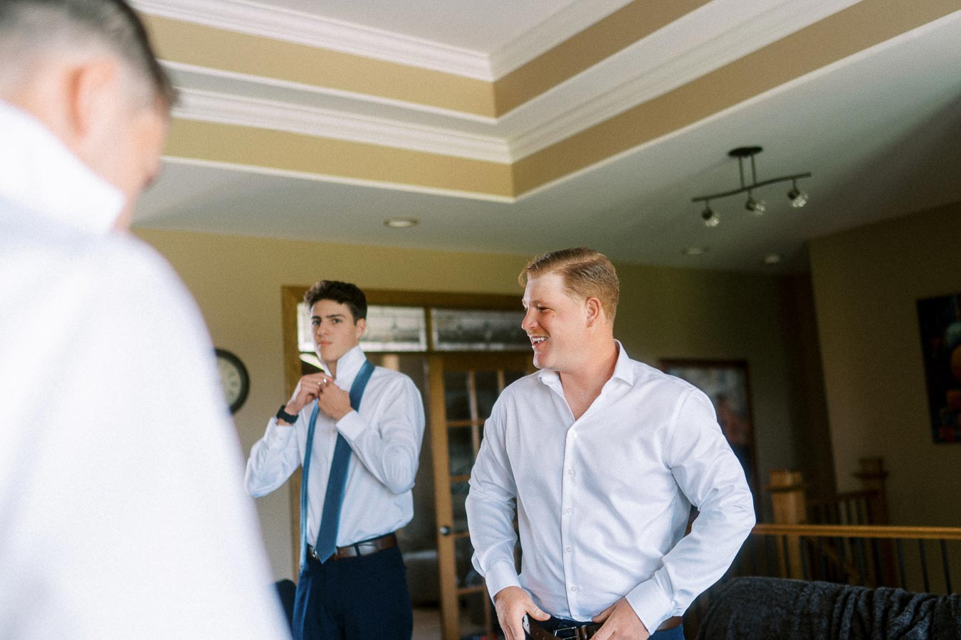 Groom and groomsman in white shirts getting ready indoors before the ceremony