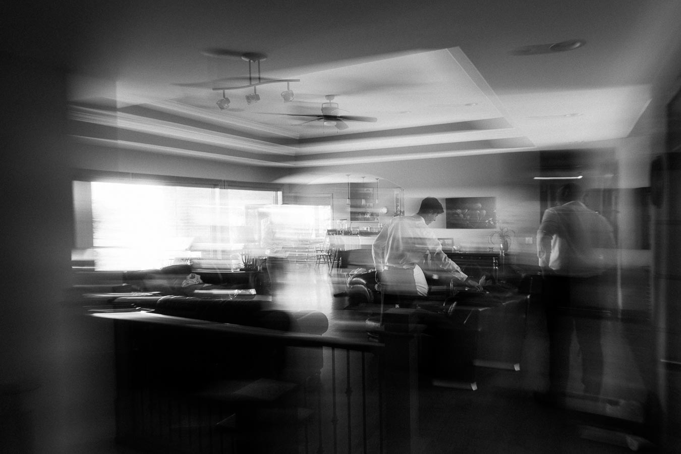 Black-and-white view of men preparing in a living room before a wedding.