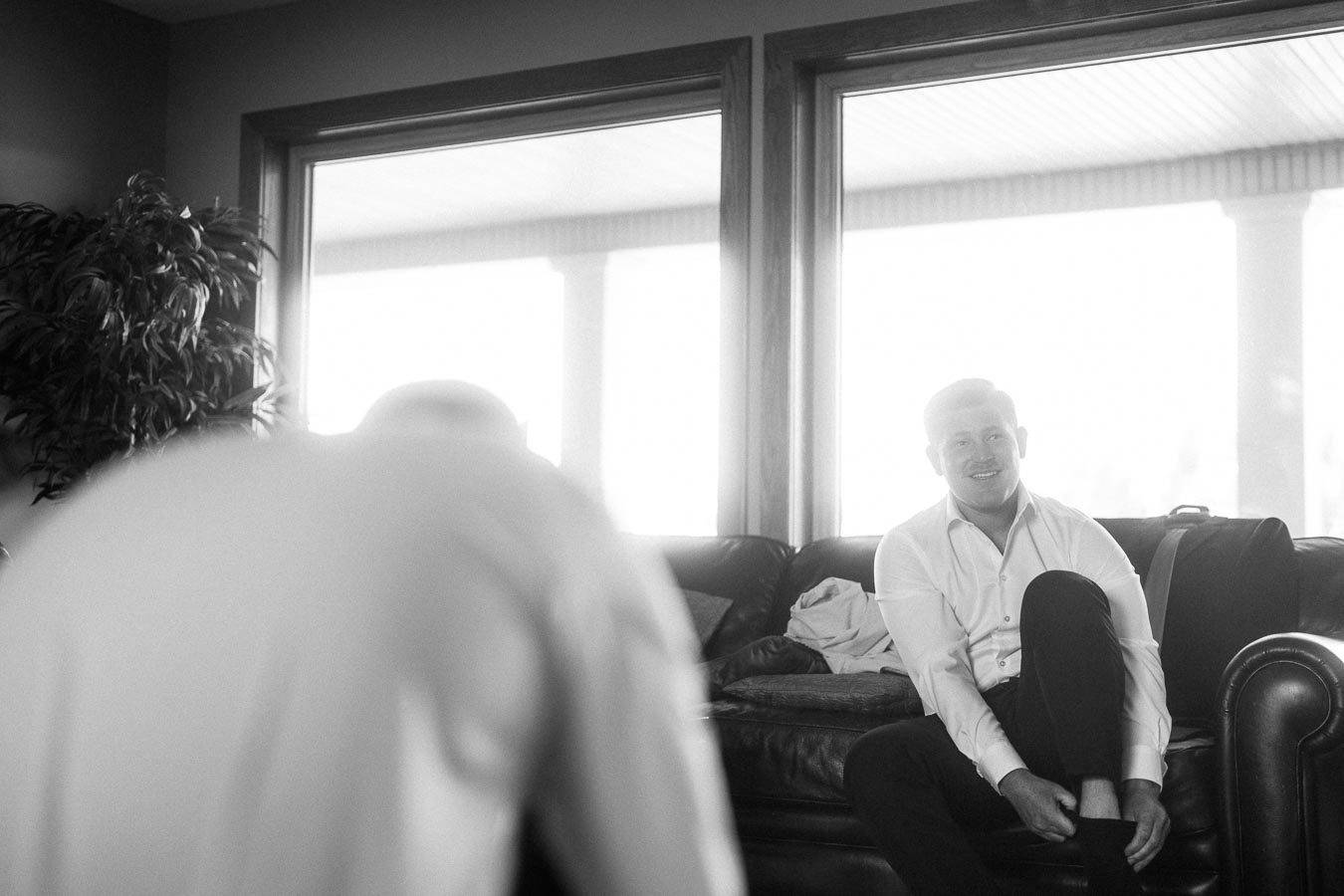 Man in a white shirt sitting on a leather couch and adjusting his sock indoors