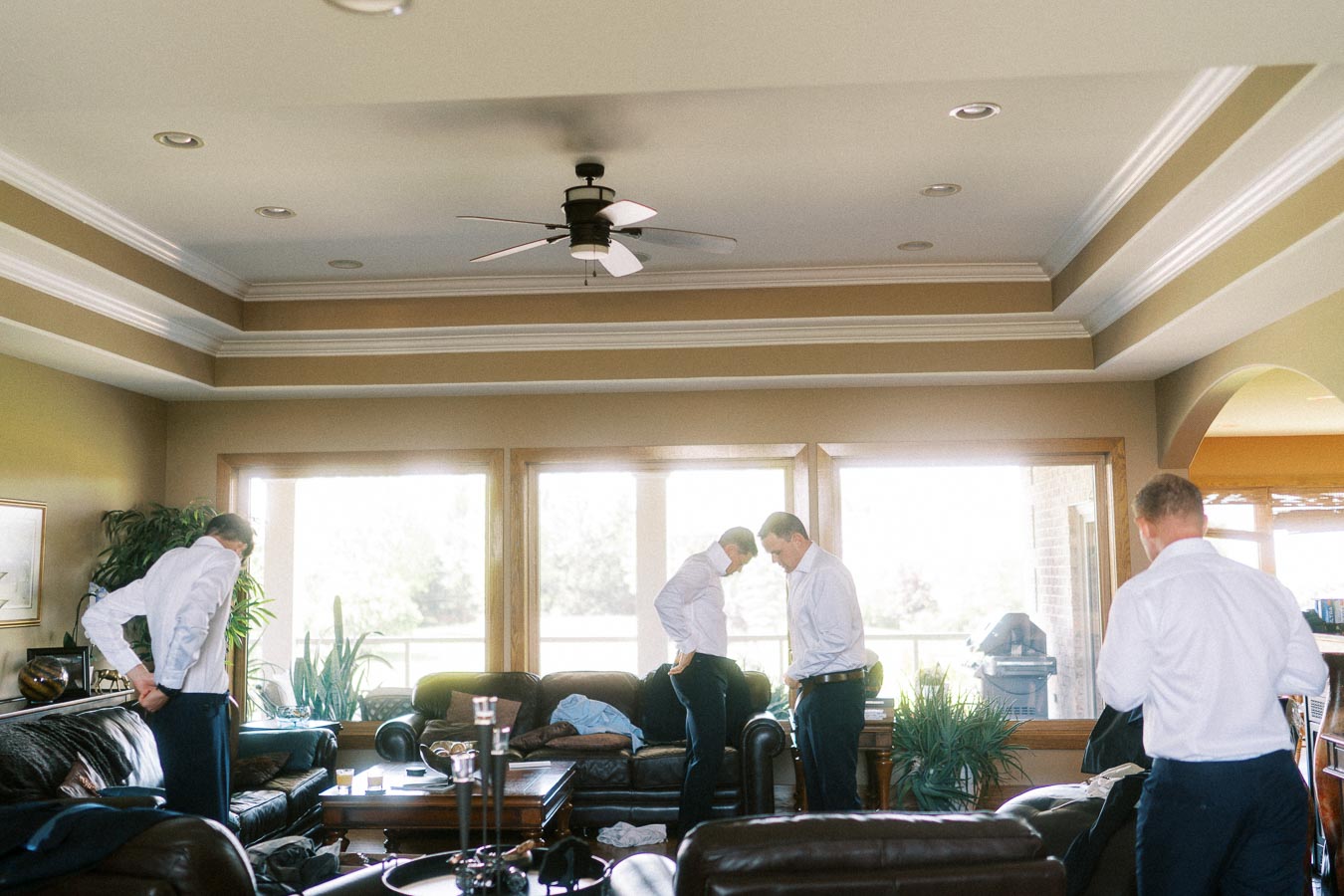Men in white shirts getting ready in a bright living room before a wedding