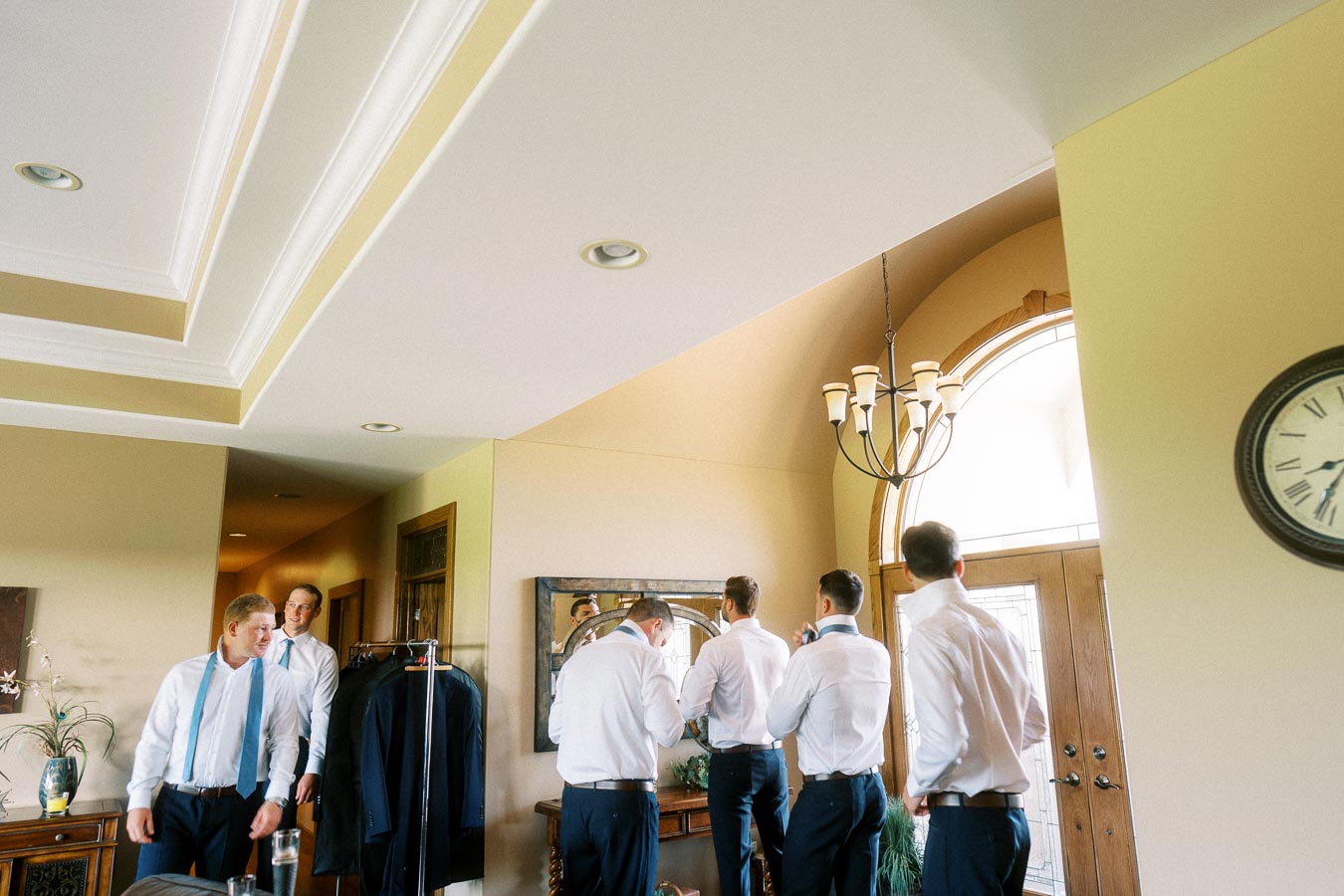 Groom and groomsmen in white shirts getting ready inside a home before a wedding.