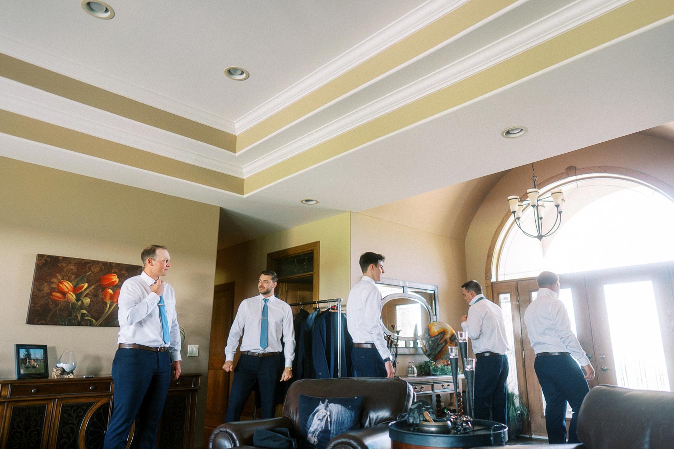 Groom and friends in white shirts and blue ties getting ready indoors before a wedding.