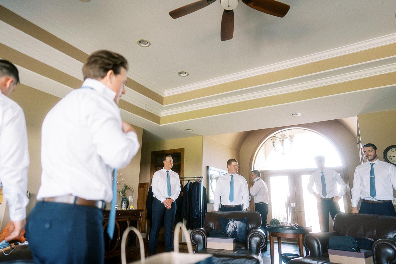 Groomsmen in white shirts and blue ties getting ready in a living room before the wedding.