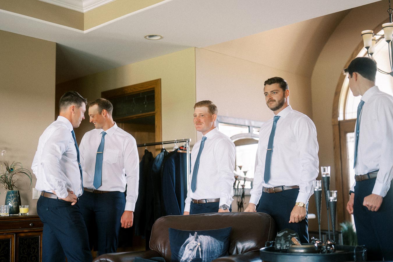 Groom and groomsmen in white shirts and blue ties gathering indoors before the ceremony