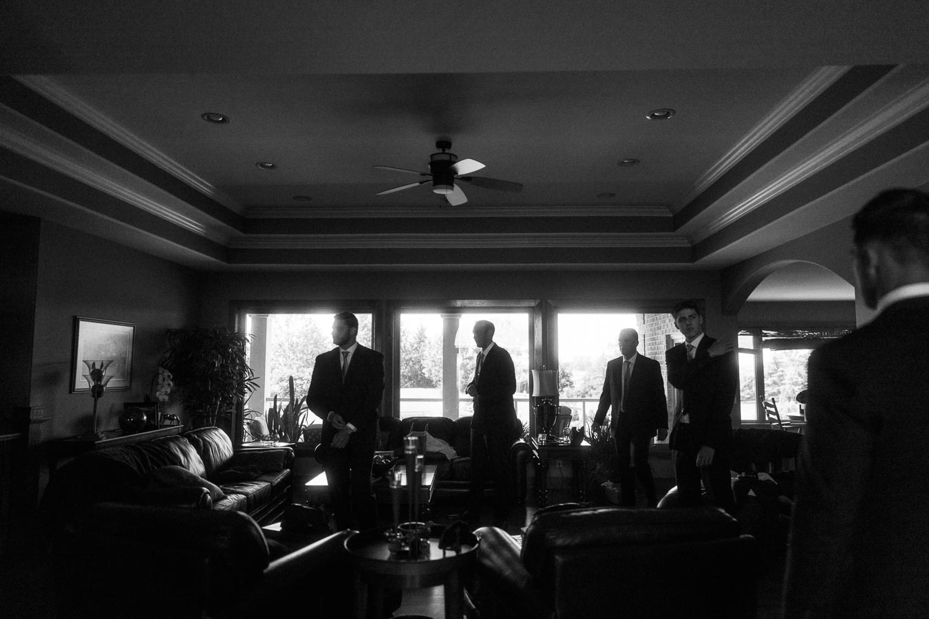 Men in suits gather in a living room during groom preparations before a wedding.