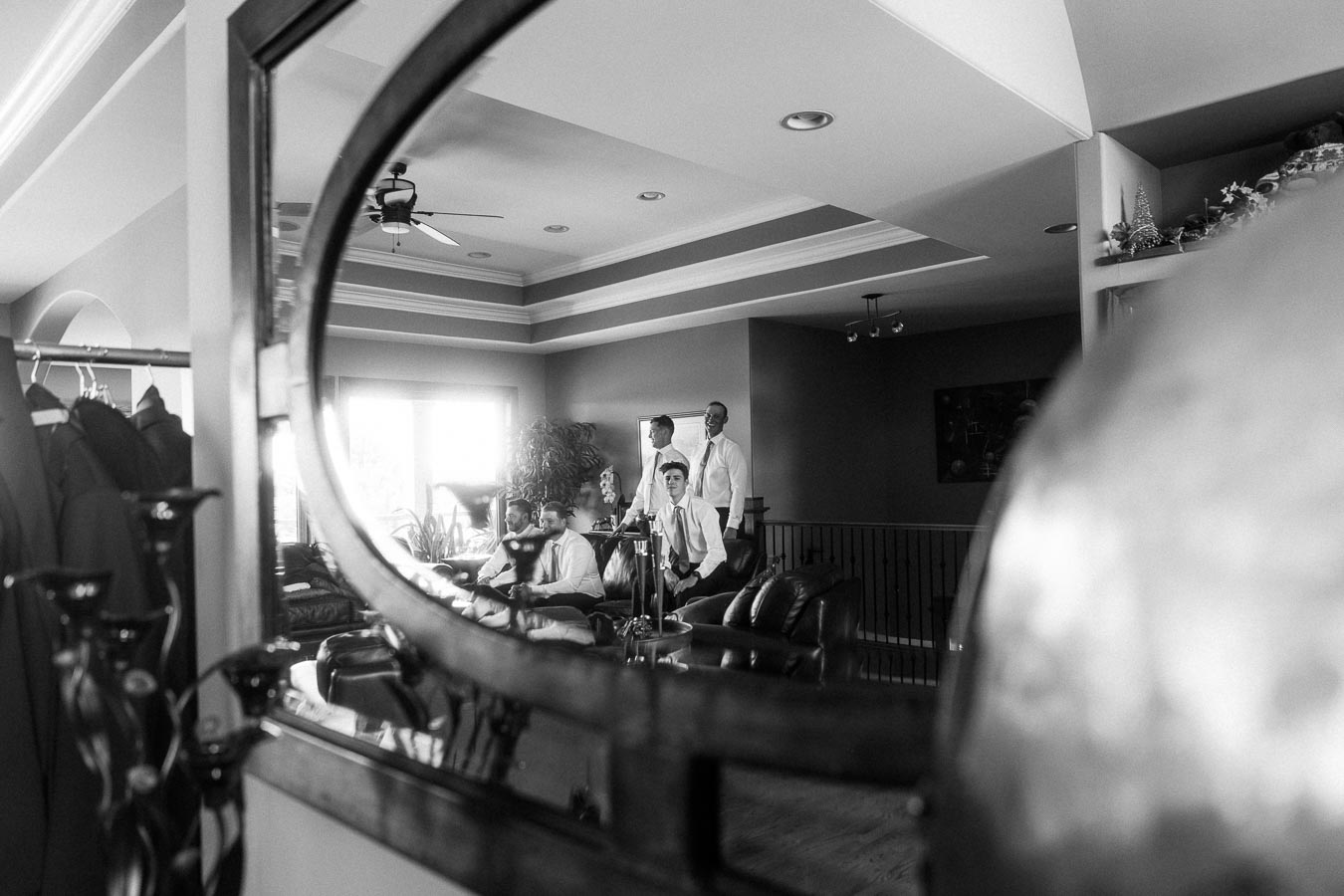 Groom and groomsmen in dress shirts reflected in a home mirror before the wedding.