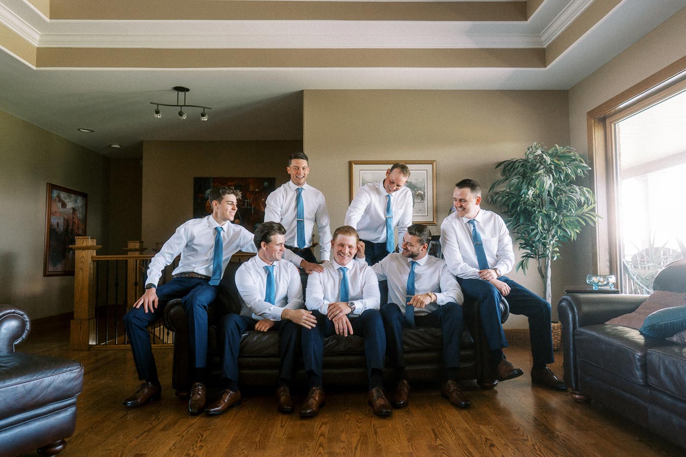 Groom and groomsmen in white shirts and blue ties posing together on a leather sofa inside a family home in Chatham-Kent, Ontario.