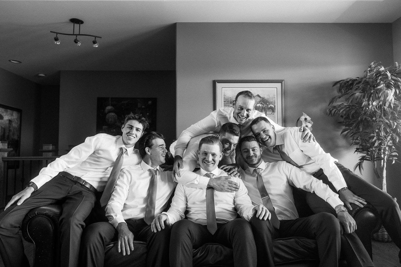 Black and white group portrait of groom and groomsmen smiling on a couch in a family home near Chatham-Kent, Ontario, Canada.