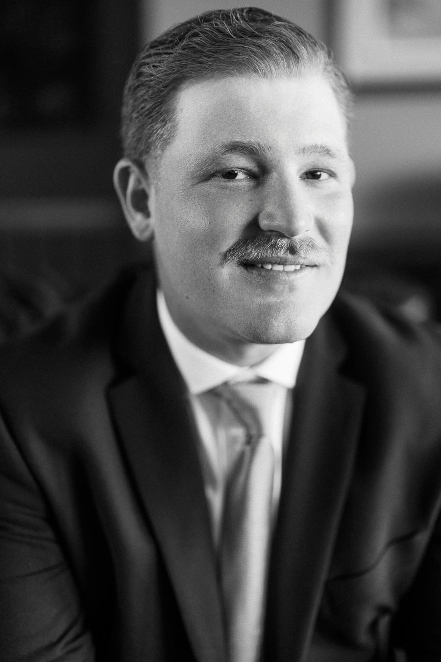 Black and white close up portrait of a groom in a suit and tie smiling softly indoors before a wedding near Chatham-Kent, Ontario.