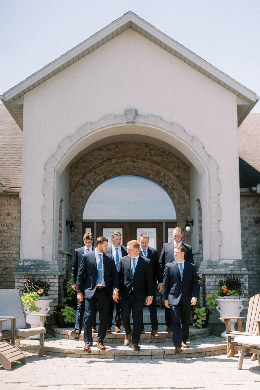 Groom and groomsmen in navy suits walking down stone steps outside a family home near Chatham-Kent, Ontario.