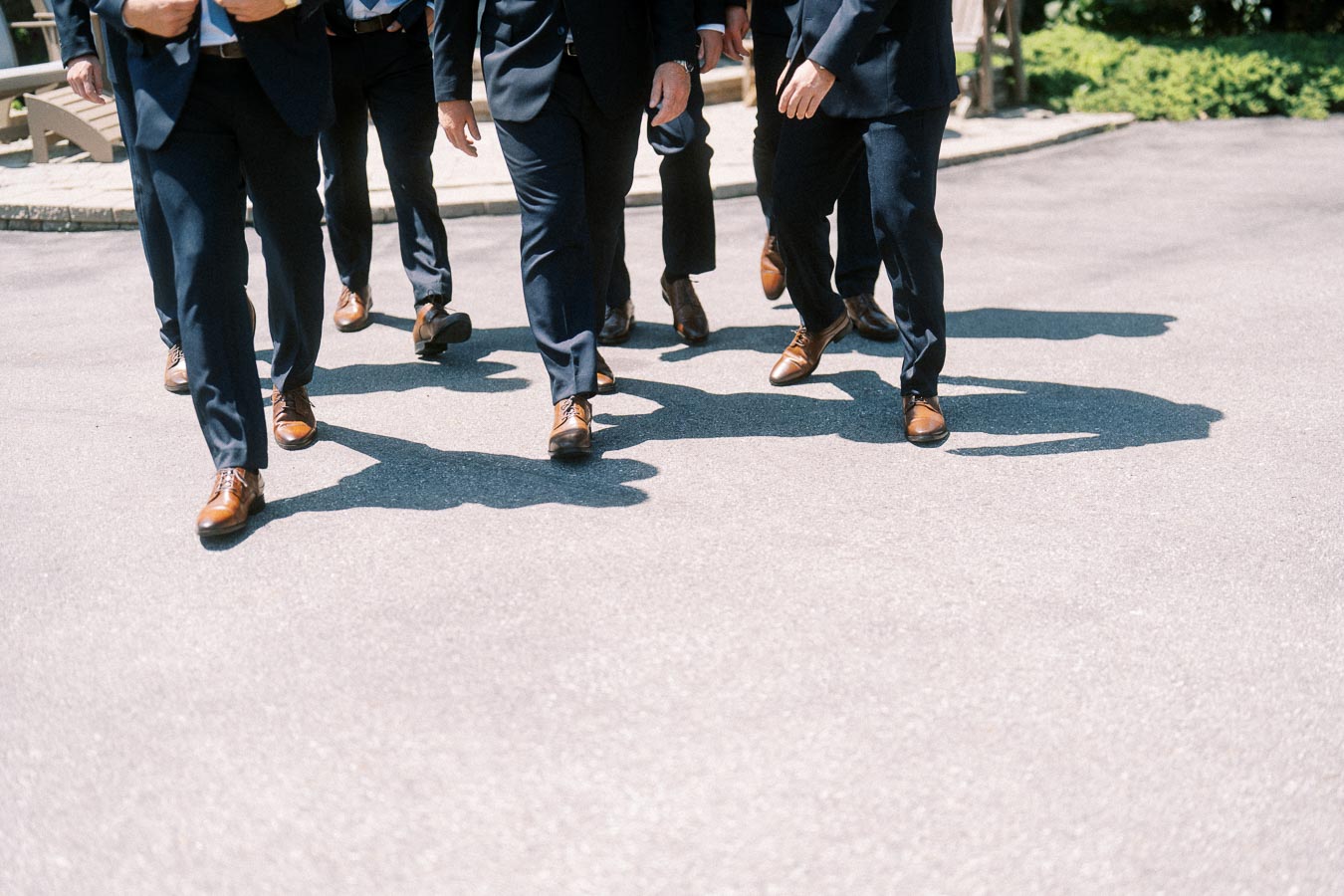 Cropped view of men in navy suits and brown dress shoes walking together on a sunny paved driveway in Chatham-Kent, Ontario.
