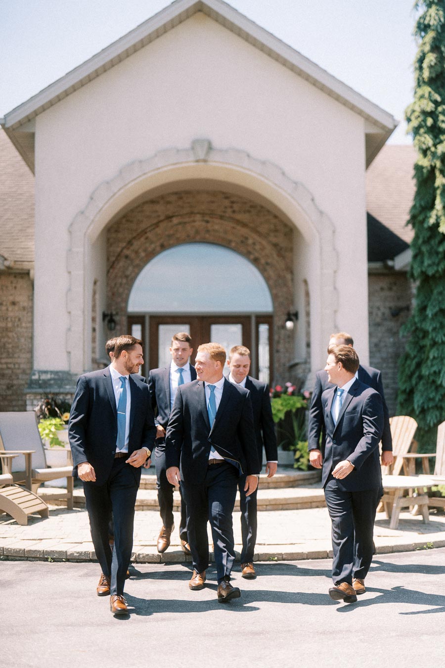 Groom and groomsmen in navy suits walking outside a family home in Chatham-Kent, Ontario before a wedding.