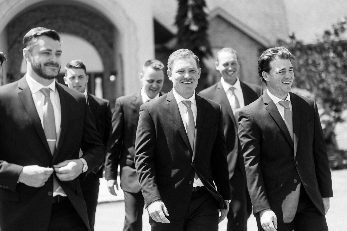 Black and white group portrait of groom and groomsmen walking outside a family home in Chatham-Kent, Ontario, Canada.