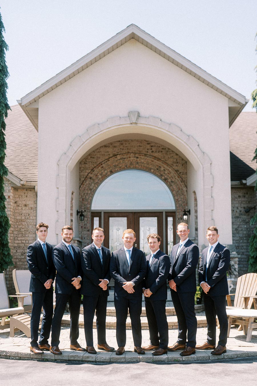 Seven men in dark suits posing in front of a brick house entrance near Chatham Kent, Ontario, Canada.