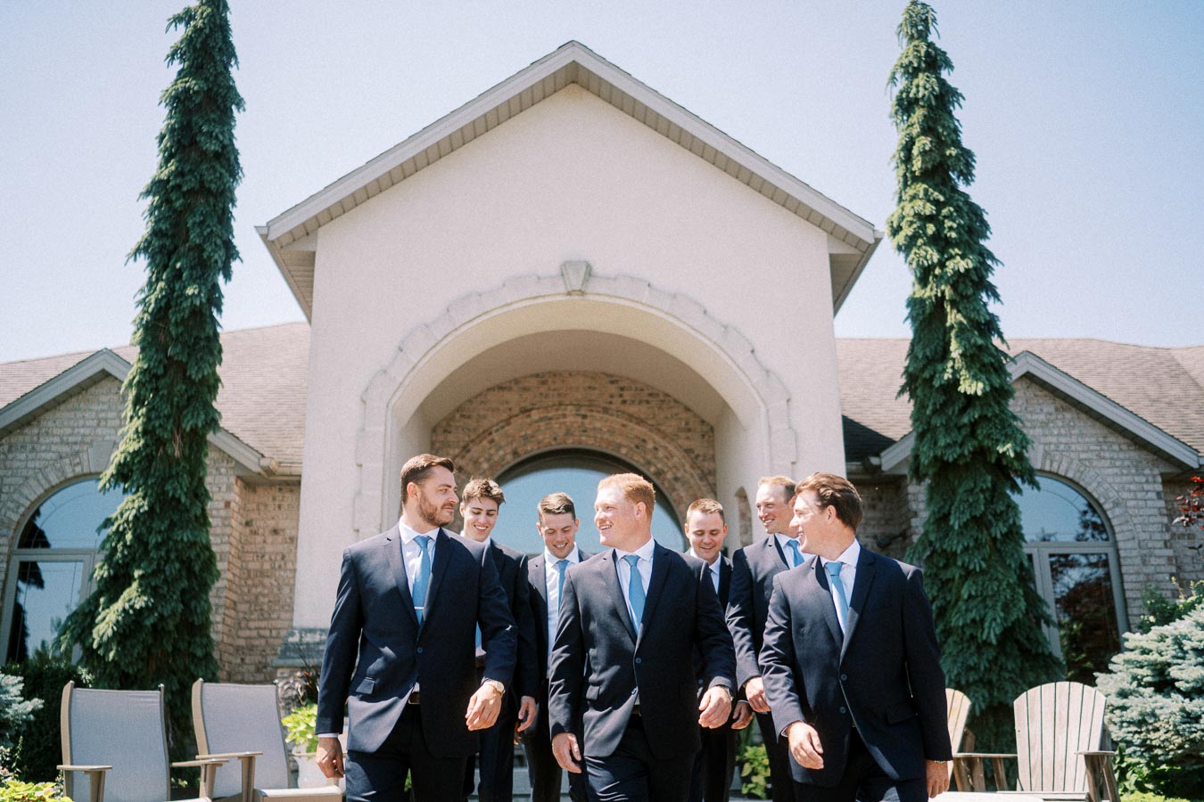 Groom and groomsmen in navy suits walking outside a large family home in Chatham-Kent, Ontario, Canada.