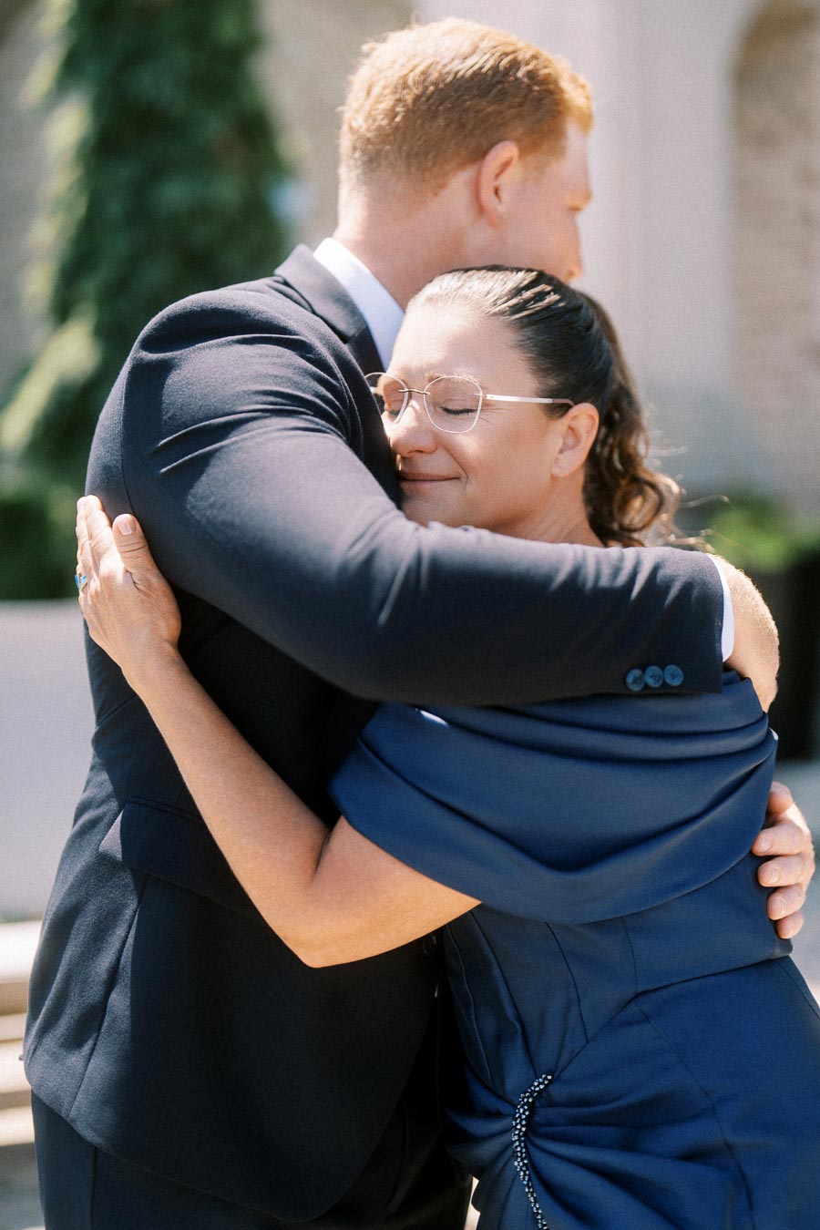Groom in a dark suit hugging his mother outdoors before a wedding near Chatham-Kent, Ontario, Canada.