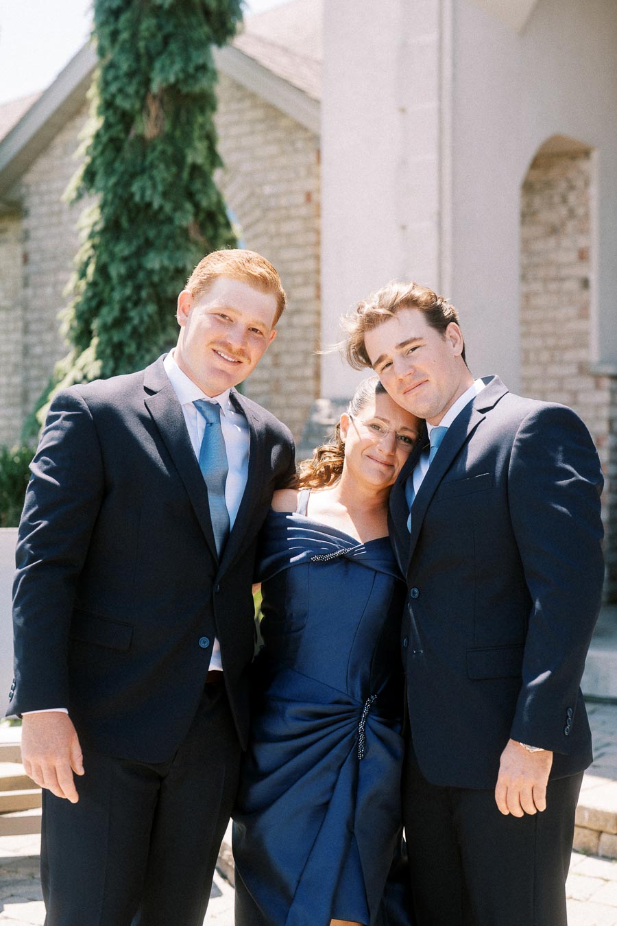 Groom with mother and brother standing together outside a stone house near Chatham-Kent, Ontario before a wedding.