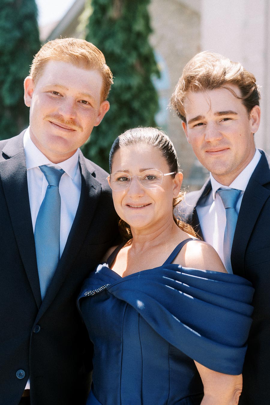 Portrait of two groomsmen in suits with their mother in a navy dress outdoors near Chatham-Kent, Ontario before a wedding.