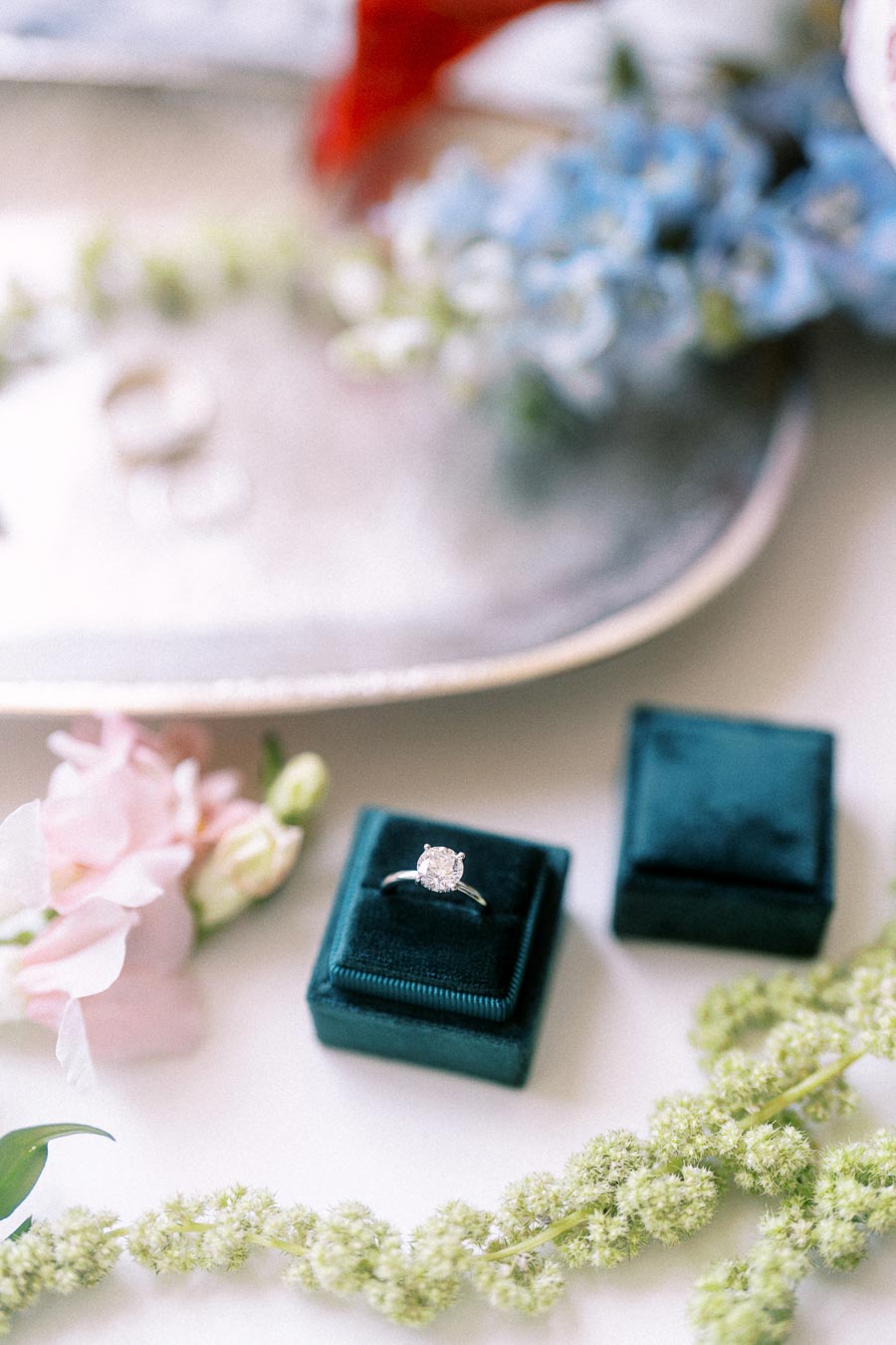 Diamond engagement ring in a teal velvet box with soft wedding flowers on a light surface in Ontario.