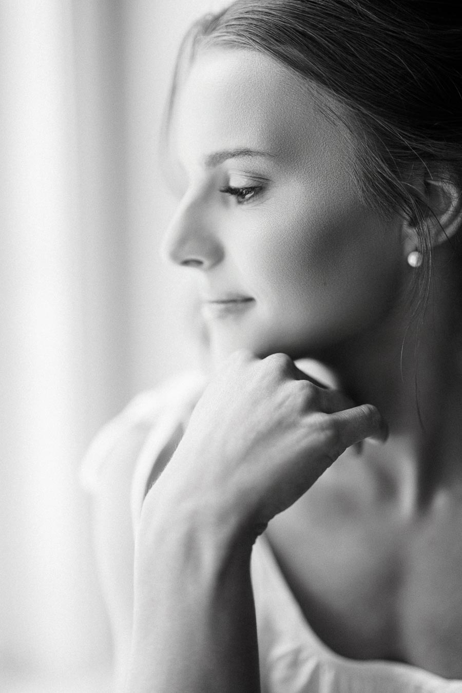 Black and white close up portrait of a bride looking toward window light with hand under chin during wedding morning in Ontario.