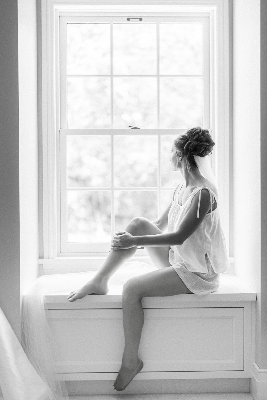 Black and white portrait of a bride sitting on a bright window seat during her wedding morning near Chatham-Kent, Ontario.