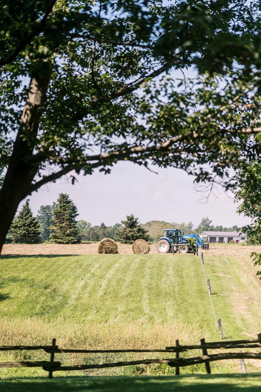 Blue tractor in a hay field with round bales on a farm near Chatham-Kent, Ontario, Canada.