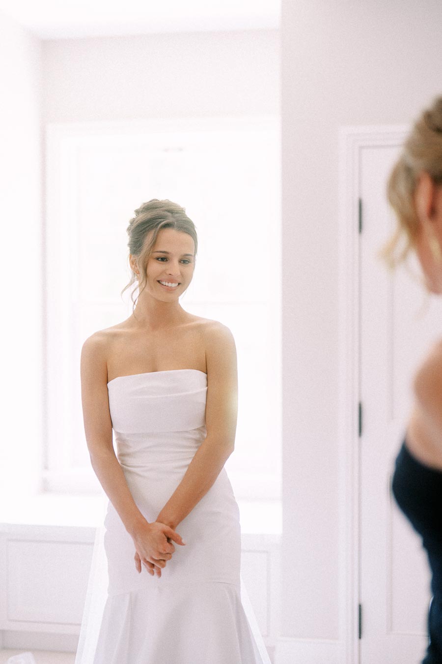Bride in a strapless white wedding dress smiling in a bright room during bridal morning preparations near Chatham-Kent, Ontario.