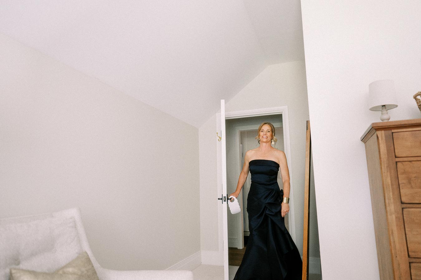 Woman in a black strapless gown enters a bright bedroom through a white door on a private farm estate near Chatham-Kent, Ontario.
